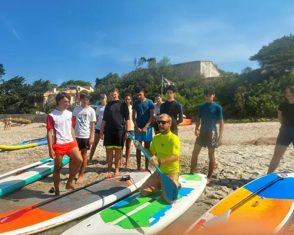 Un groupe d'adolescents et un moniteur sur une plage avec des planches de paddle.