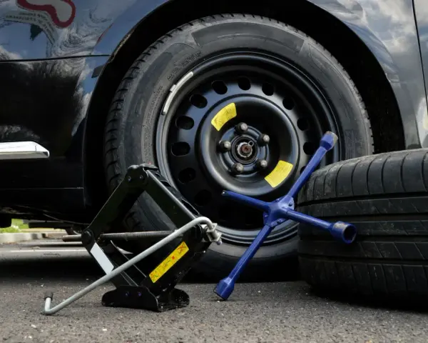 Kit per cambiare una ruota: cric, chiave a stella e ruota di scorta accanto a un'auto nera.