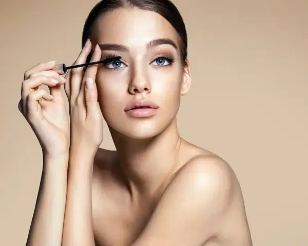 Donna con occhi azzurri applica mascara. Scopri come togliere il mascara waterproof senza irritare la pelle.