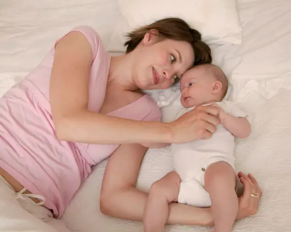 Mama patrzy z miłością na swoje 5 tygodniowe dziecko leżące obok niej na łóżku.