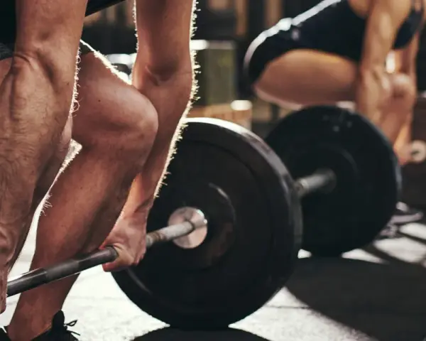 Personer lyfter skivstång i gym. Frågan "hur lång tid tar det att bygga muskler" besvaras med konsekvent träning.