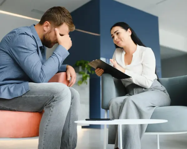 Mężczyzna w stresie podczas sesji, która może być częścią terapii uzależnień online. Terapeutaka notuje.