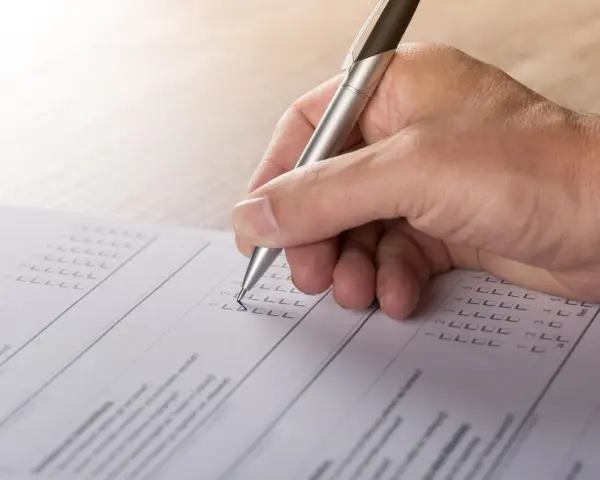 Dłoń z długopisem wypełnia formularz, zaznaczając odpowiedzi. To część procesu tworzenia wykazu majątku.