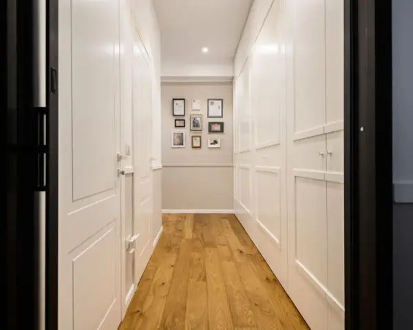 Corridoio con parquet e armadi bianchi. Un'idea per come dividere un corridoio lungo con porte e quadri decorativi.