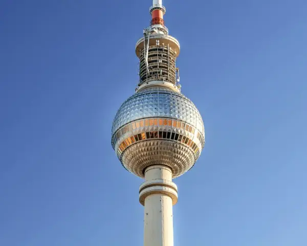 Die Torre della televisione di Berlino ragt in den blauen Himmel. Ihre kugelförmige Spitze mit Fenstern reflektiert das Licht.