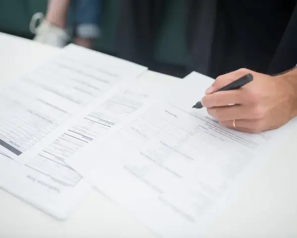 Ręka klienta podpisuje dokumenty ubezpieczeniowe. Agent ubezpieczeniowy czeka na zakończenie formalności.