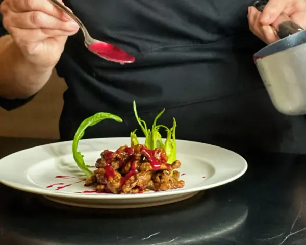 Chef decora un piatto di straccetti di manzo con una salsa rossa brillante, guarnendo con verdure verdi.