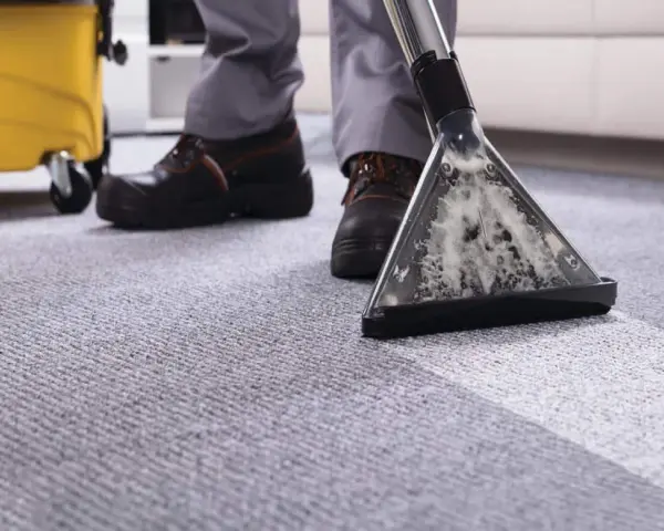 A person demonstrates how to clean a carpet using a professional carpet cleaner, leaving a fresh, clean path.