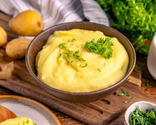 Cremiger Kartoffelbrei, perfekt zubereitet im Thermomix, garniert mit Petersilie. Dazu frische Kartoffeln und ein Glas Milch.