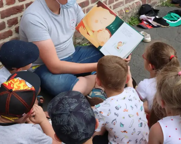 Un animateur lit un livre illustré à des enfants assis en cercle. L'image évoque un moment de partage et d'apprentissage, comme un diplôme animation.