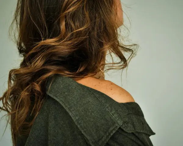 Spalle scoperte e capelli castani mossi, un dettaglio di donne con pochi capelli che incornicia il volto.