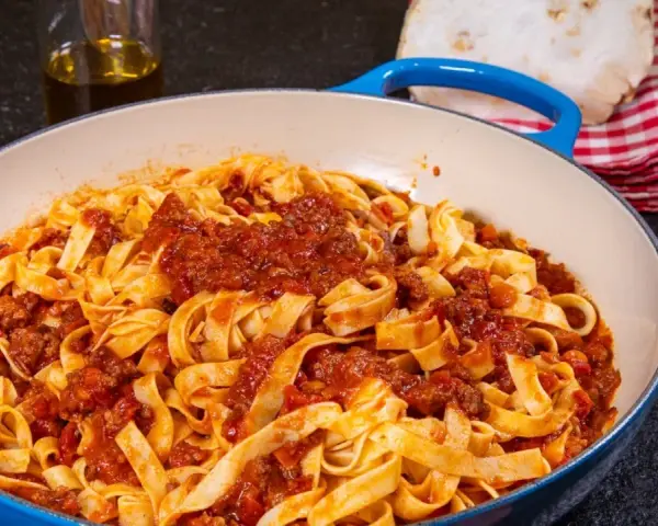Herzhafte Tagliatelle mit einer reichhaltigen alla bolognese Sauce in einer blauen Pfanne, bereit zum Servieren.