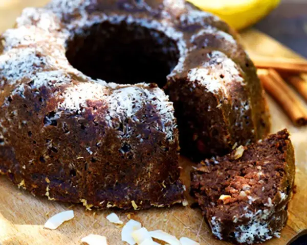 En saftig banankaka med choklad, toppad med kokosflingor. En bit är uppskuren och visar den rika, mörka insidan.