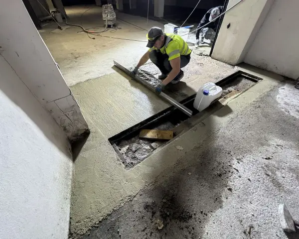 Pracownik wykonuje naprawę posadzki betonowej, wyrównując świeżą masę za pomocą łaty.