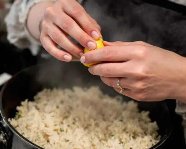 Des mains pressent un citron sur une soupe de riz fumante, ajoutant une touche de fraîcheur à ce plat réconfortant.