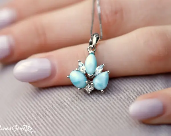 Un ciondolo con una splendida larimar pietra, incastonata con zirconi, adagiato su una mano con unghie lilla.