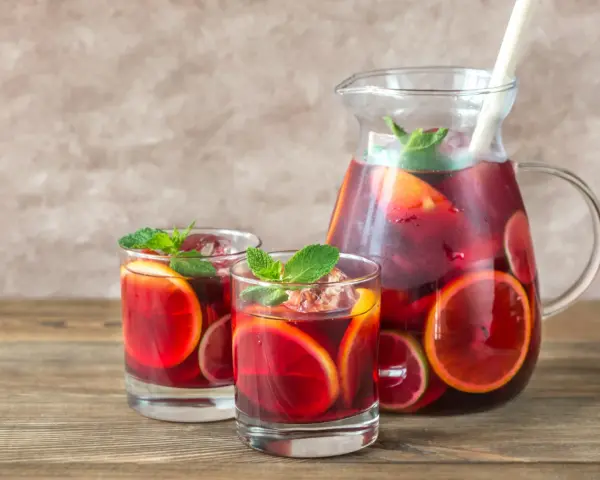 Dwa szklanki i dzbanek pełne orzeźwiającej Sangrii czerwonej z plasterkami pomarańczy i limonki, ozdobione miętą. Idealny wybór na lato!