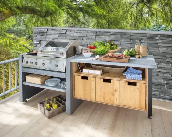 Moderne Grillecke im Garten mit Edelstahlgrill, Arbeitsplatte, Holzschränken und frischen Zutaten. Tolle Garten Ideen für Grillmeister.