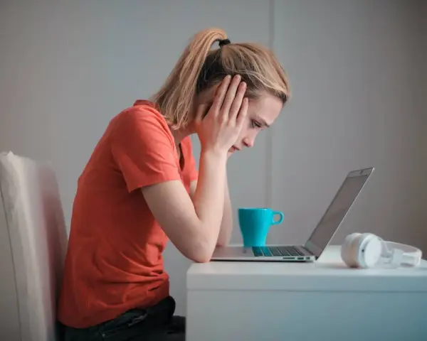 Zmartwiona kobieta przy laptopie, zastanawia się, czy porzucenie pracy wlicza się do emerytury. Na biurku kubek i słuchawki.