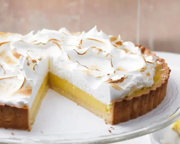 Eine köstliche Tarte au Citron mit fluffiger Baiserhaube, die auf einem Tortenständer präsentiert wird.