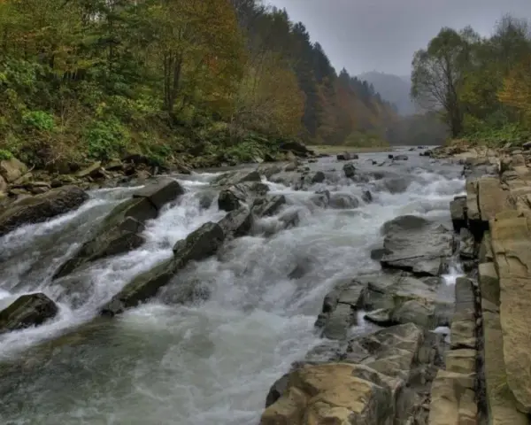 Bieszczady w jesiennej odsłonie. Rzeka wartko płynie wśród kamieni, tworząc sine wiry. Las na zboczu mieni się barwami.