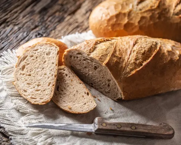 Chleb z kaszy jaglanej, pokrojony na kromki, leży na lnianej serwetce obok noża.