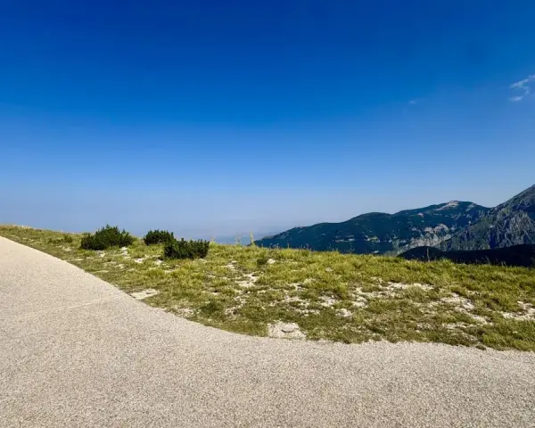 Sentiero ghiaioso verso la cima Blockhaus, con prati verdi e montagne sullo sfondo sotto un cielo azzurro.