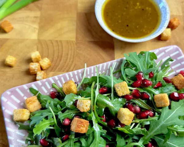 Frischer Rucola Salat mit Granatapfelkernen und Croutons, dazu ein Dressing.