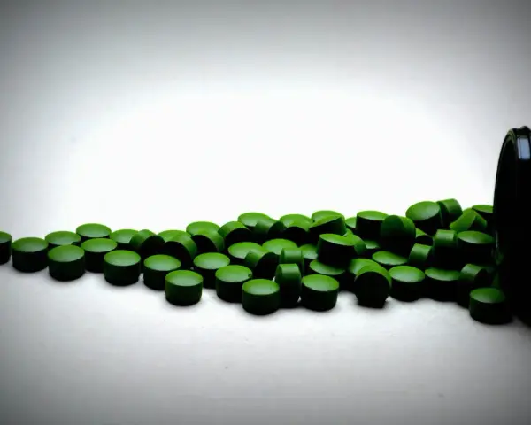 Zielone tabletki chlorelli rozsypane z czarnego pojemnika. Kiedy je brać: chlorella rano czy wieczorem?