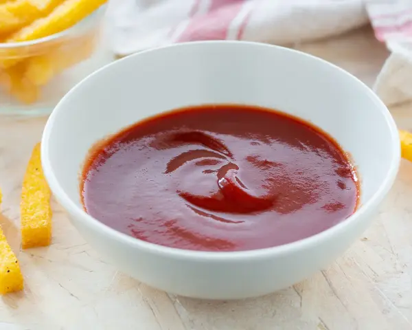 Una ciotola di ketchup fatto in casa, pronto per intingere bastoncini di polenta dorati.