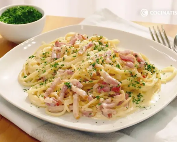 Espaguetis con nata, cubiertos de trocitos de bacon y perejil picado. Un plato cremoso y delicioso.