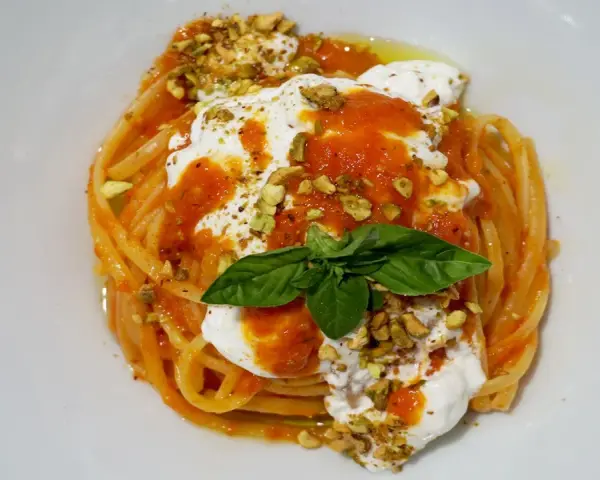 Un piatto invitante di pasta con stracciatella, salsa di pomodoro, pistacchi tritati e una foglia di basilico fresco.
