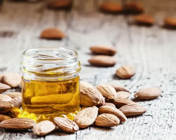 Aceite de almendras para que sirve: un frasco de aceite dorado rodeado de almendras sobre madera rústica.