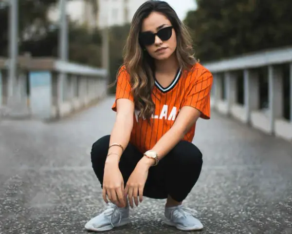 Mujer con estilo smart casual, con camiseta naranja a rayas, pantalones negros y zapatillas deportivas.