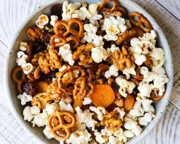 A bowl of delicious walnut trail mix, featuring popcorn, pretzels, dried cranberries, and apricots.