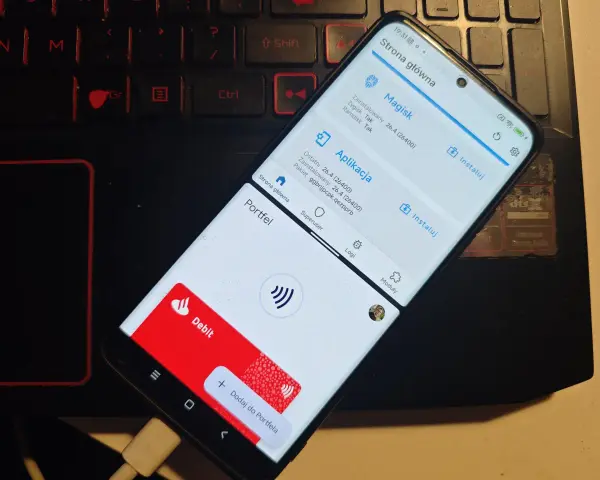 Telefon z aplikacją Magisk, która jest kluczowa, by dowiedzieć się, jak zrootować telefon. Widoczny też portfel z kartą płatniczą.