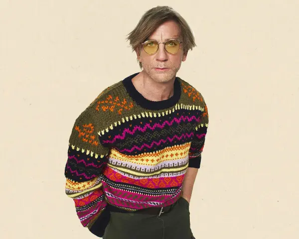 Mann mit gelber Brille trägt einen bunten Pullover aus Wolle, schleudern von Mustern.