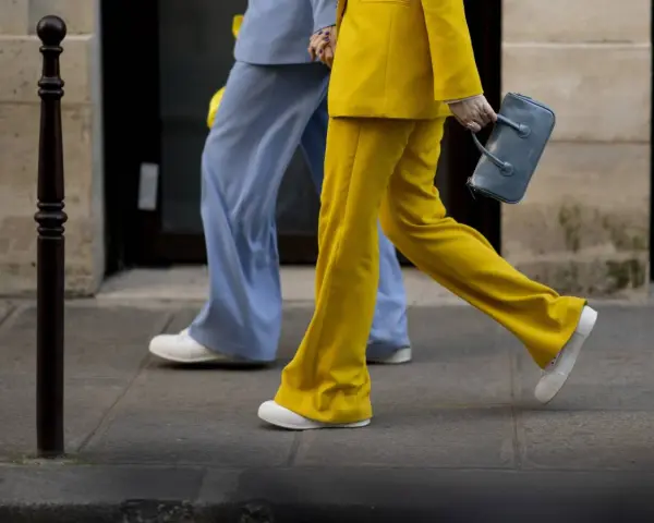 Un outfit tailleur con sneakers, giallo brillante e azzurro polvere, camminano sul marciapiede.
