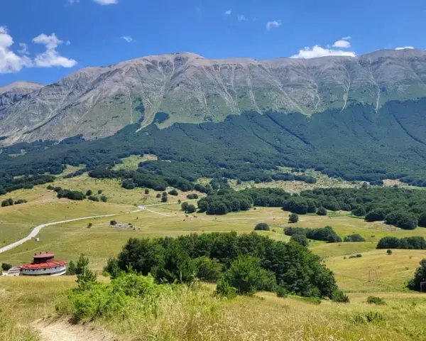 Vasta distesa verde ai piedi del monte Mileto, con un edificio circolare rosso e una strada tortuosa.