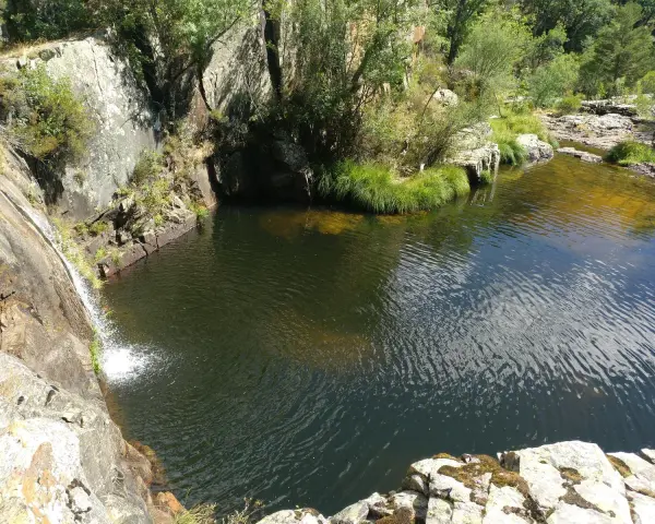 Las pozas negras de Cantalojas, un remanso de paz rodeado de vegetación y rocas, con una cascada cayendo en el agua oscura.