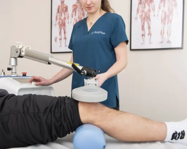 Fizjoterapeuta wykonuje zabieg rehabilitacyjny na kolanie pacjenta za pomocą specjalistycznego urządzenia.