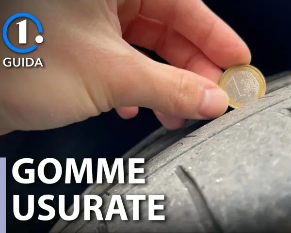 Una mano tiene una moneta da 1 euro per controllare il battistrada di pneumatici usurati. La guida mostra come verificare la sicurezza.
