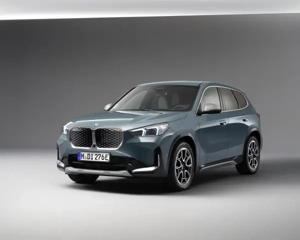 BMW iX1 w kolorze zielonym, widok z przodu, na szarym tle.