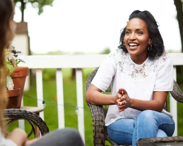 Two women are sitting on a porch, one animatedly sharing the gospel with the other.