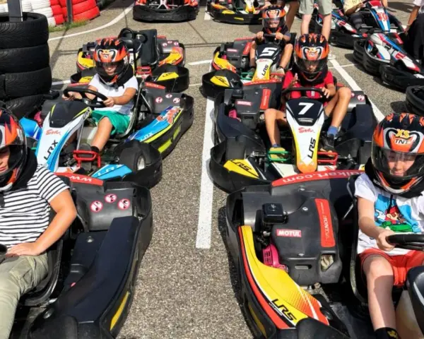Des enfants casqués prêts pour une course de colo karting, le sourire aux lèvres, impatients de démarrer.