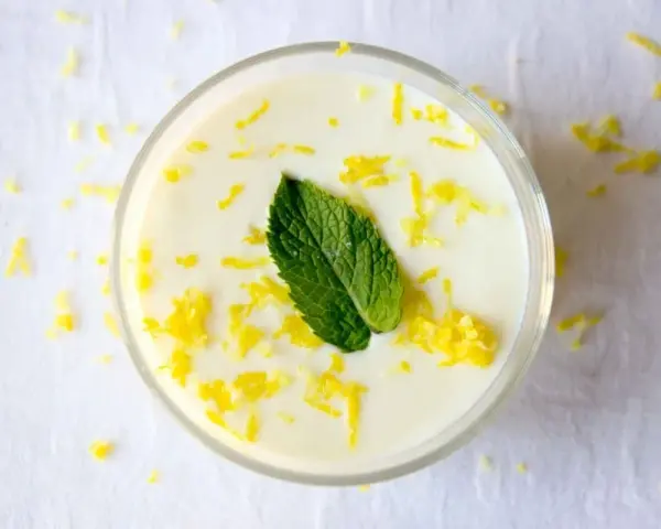 Delicioso mousse de limón, adornado con ralladura de limón y una hoja de menta fresca, servido en un vaso transparente.