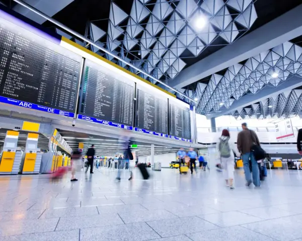 Tablica odlotów na lotnisku, ludzie z bagażami spieszą na boarding.