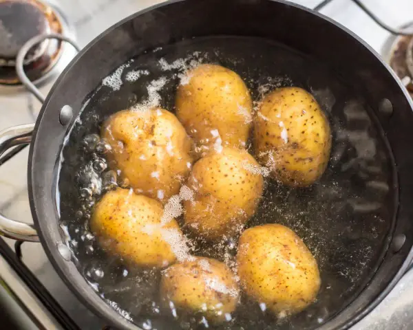 Mehrere ganze Kartoffeln kochen in einem Topf mit sprudelndem Wasser auf dem Herd.