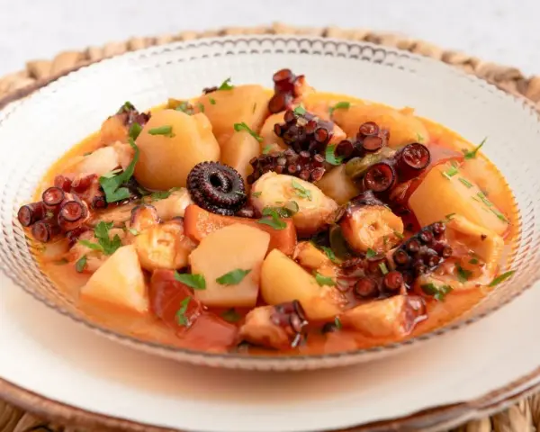 Un delicioso pulpo a la mugardesa, con patatas tiernas y un sofrito sabroso, adornado con perejil fresco.