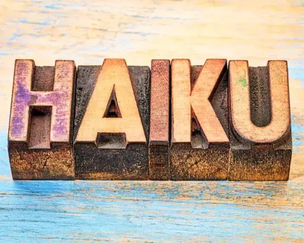 Träbokstäver bildar ordet "HAIKU" på en sliten träyta. En hyllning till den korta, poetiska formen.